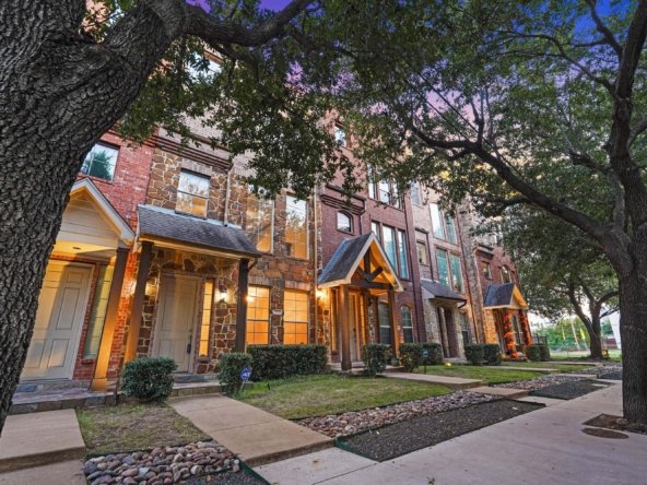 A charming three-bedroom townhome nestled on a picturesque tree-lined street in the Townhomes of Cityplace. It is buffered from the street by a front yard, two decorative stone borders, and a spacious sidewalk. The large pathway is often enjoyed by dog walkers, joggers, and neighbors out for a stroll, creating a welcoming and vibrant atmosphere.