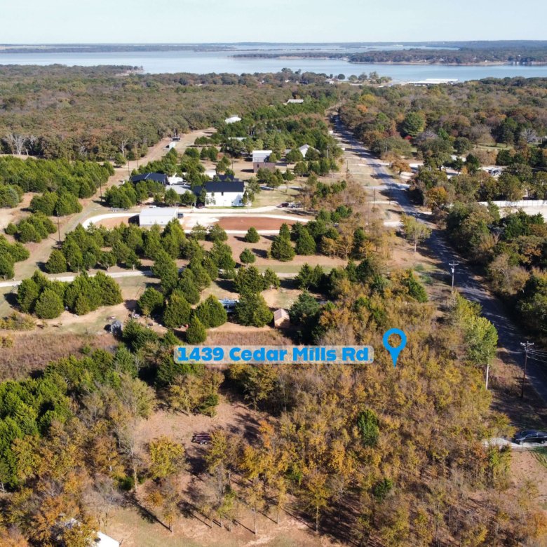 Aerial drone view showing the location of 1439 Cedar Mills Road in Gordonville, Texas, highlighted with a map pin and label, with the unimproved 1-acre lot surrounded by mature trees and nearby homes, and Lake Texoma visible in the background to illustrate the property’s close proximity to the lake and Cedar Mills Marina area.