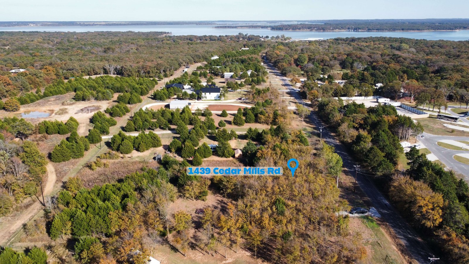 Aerial drone view showing the location of 1439 Cedar Mills Road in Gordonville, Texas, highlighted with a map pin and label, with the unimproved 1-acre lot surrounded by mature trees and nearby homes, and Lake Texoma visible in the background to illustrate the property’s close proximity to the lake and Cedar Mills Marina area.
