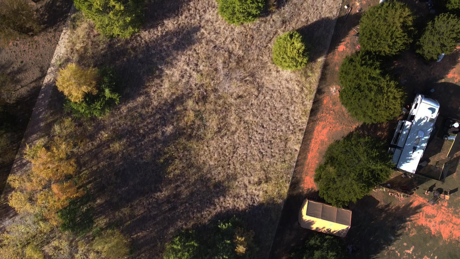 Shaded aerial view of the open clearing beyond the first set of trees on the 1-acre lot at 1439 Cedar Mills Road, Gordonville, TX, illustrating usable space within the wooded landscape.