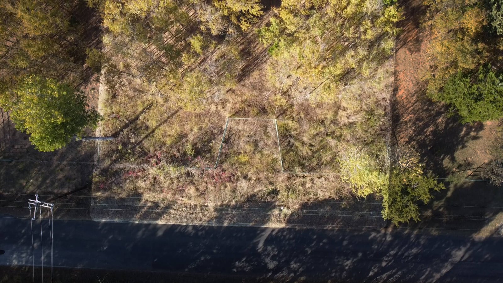 Aerial view of the gated entrance and road frontage of the 1-acre lot at 1439 Cedar Mills Road in Gordonville, Texas, with highlighted property boundaries and visible power lines along the road.