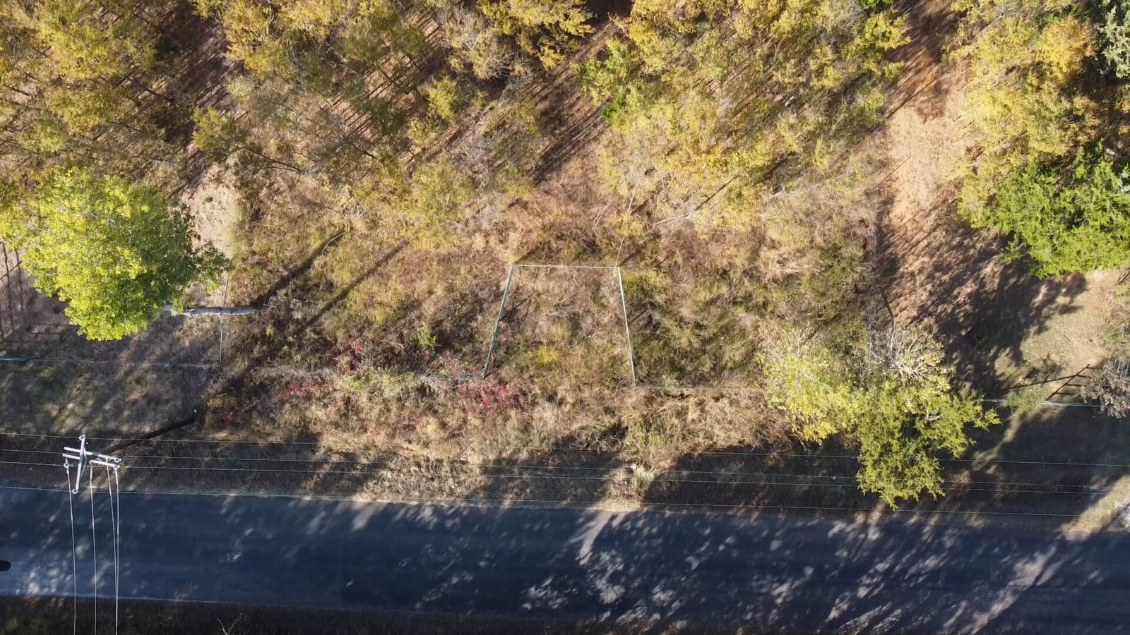 Overhead drone image of the road frontage and gated entrance to the unimproved 1-acre lot at 1439 Cedar Mills Road in Gordonville, TX, showing boundary markers, fencing, and direct access from Cedar Mills Road.