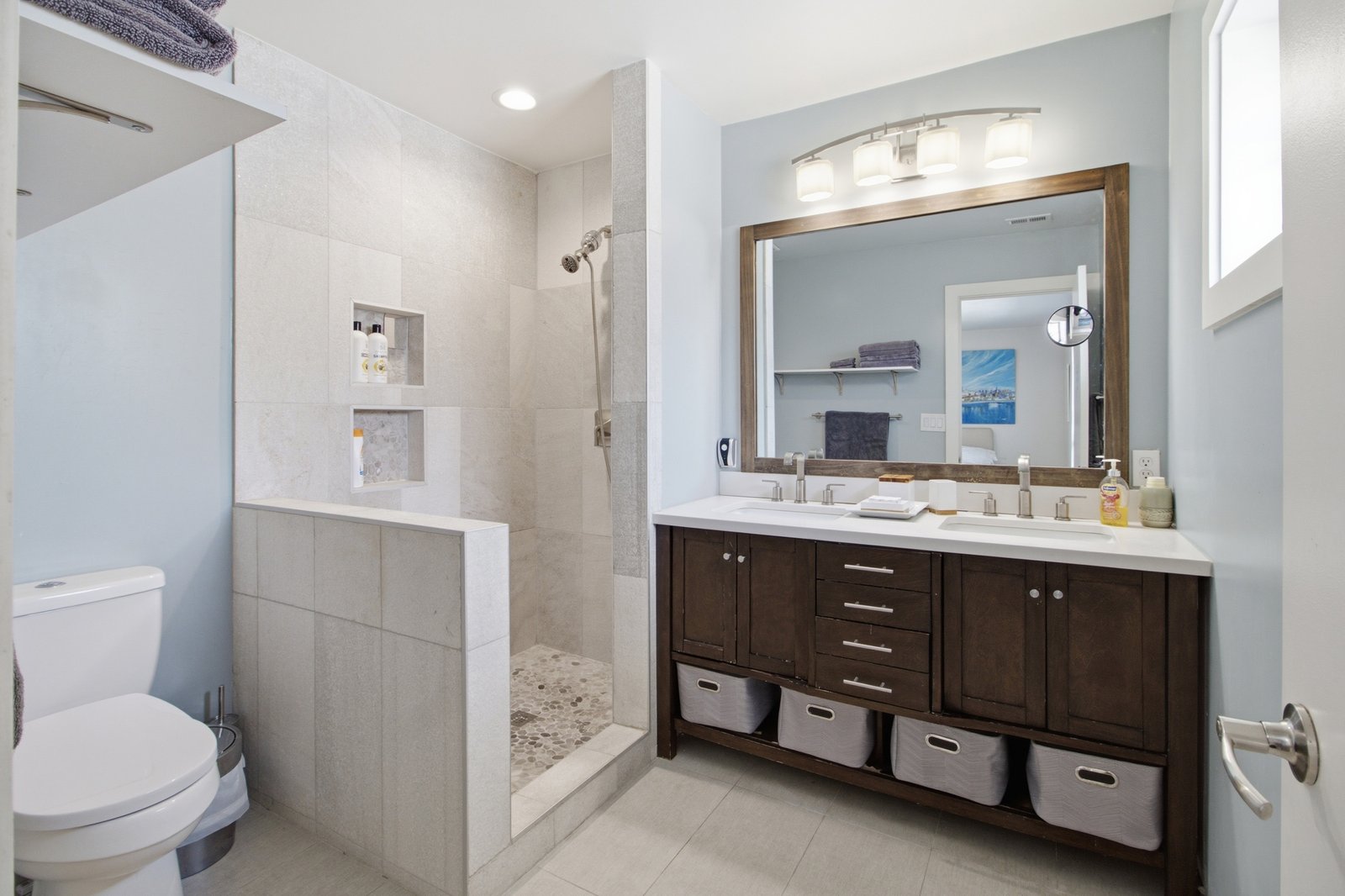 19_img_0065 The primary ensuite bathroom features a spacious walk-in shower with tile surround, pebble-style flooring, and recessed storage niches. A double-sink vanity with dark wood cabinetry, generous counter space, and open shelving provides everyday convenience in a contemporary setting.