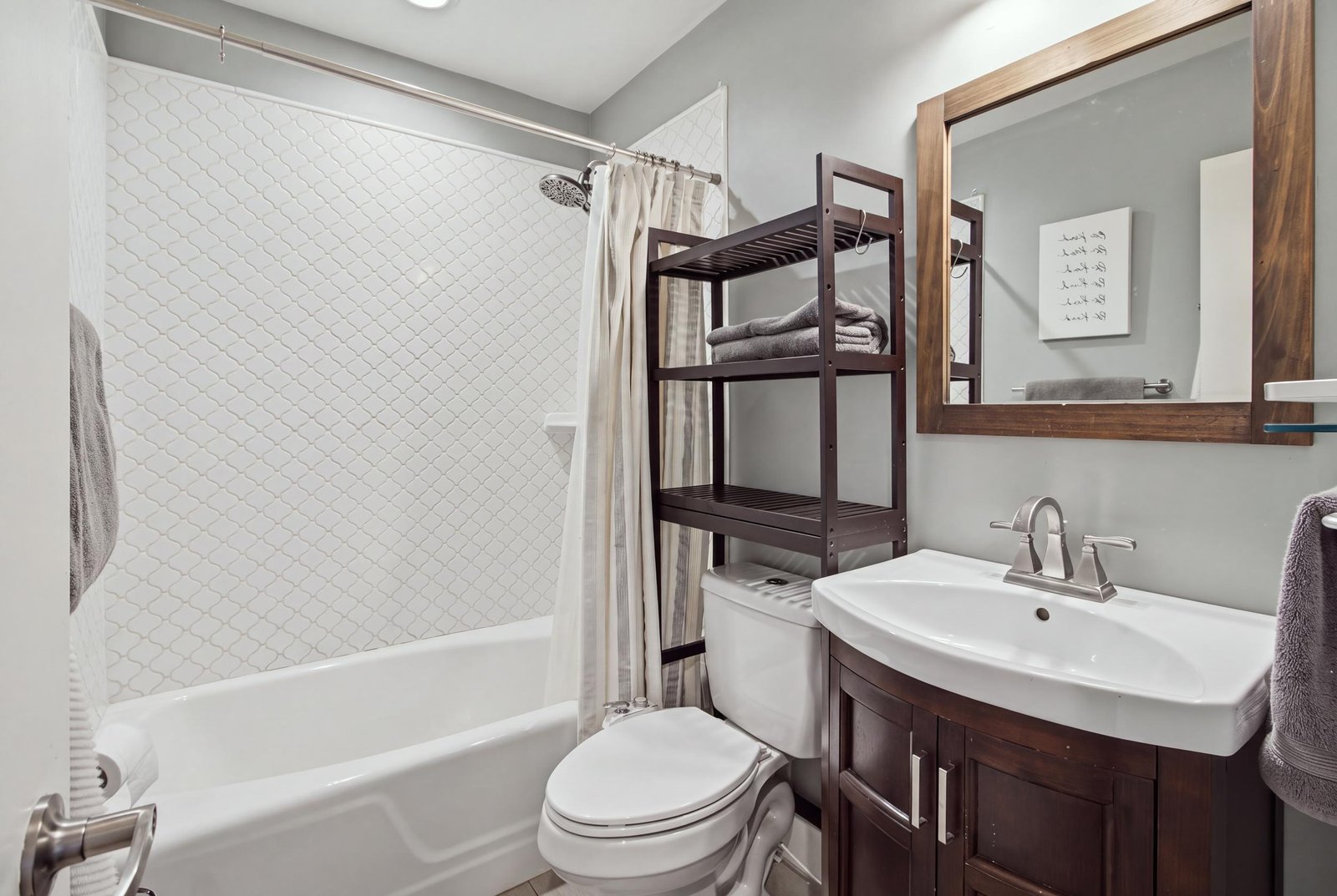 45_img_9746_reedit_e1d4a19d The second full bathroom is conveniently located off the hallway, serving both secondary bedrooms and guests. Features include a tub and shower combination with decorative tile surround, a dark wood vanity, and a coordinating framed mirror.