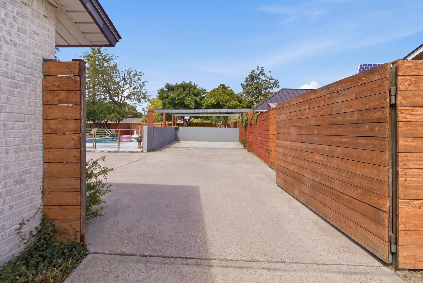 52_img_0146_reedit_5e67aa5d Beyond the horizontal wood privacy gate, the extended driveway opens into a generous paved parking area, offering convenient additional parking for vehicles and guests. The wood fencing complements the home's contemporary styling while providing separation from the street. With the swimming pool and outdoor entertaining areas nearby, this flexible space is especially convenient when hosting larger gatherings.