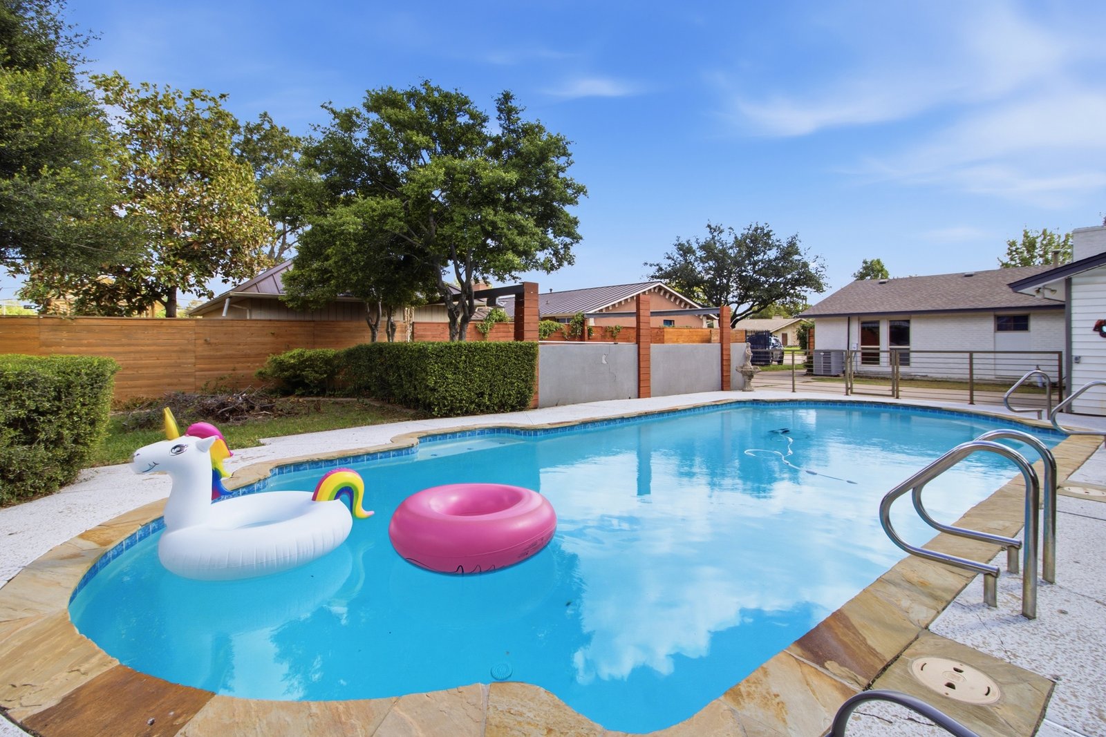 59_img_0224 Who’s ready for a pool party? The sparkling swimming pool takes center stage, with colorful floats adding a playful touch to this backyard retreat. Mature trees, neatly trimmed hedges, and attractive wood privacy fencing create a lush, inviting setting. Beyond the pool, an additional grassy area offers even more outdoor space to enjoy, whether relaxing in the sunshine or gathering with friends and family.
